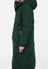Grön quiltad lång jacka med huva, featuring en framdragkedja, sidofickor och mönstrade sömmar. Slät tygtextur.