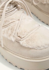 Beige plush sneakers with a suede finish, featuring flexible laces, a thick sole, and soft, textured accents on the upper.