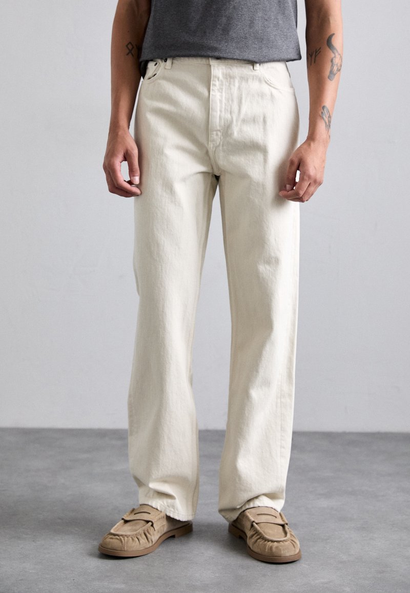 Beige bomullsbukser med rett ben-passform og subtil tekstur, kombinert med lysebrune semskede sko.
