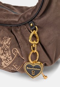 Bolsa de camurça castanha com acabamento em pele preta, acessórios dourados e um pingente em forma de coração com a inscrição "Juicy Couture".