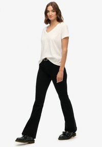 Wit T-shirt met korte mouwen en V-hals, gecombineerd met zwarte uitlopende jeans en zwarte veterschoenen. Eenvoudig ontwerp, zachte textuur en casual pasvorm.