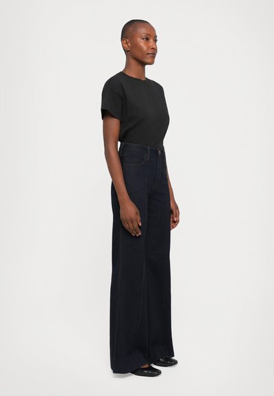Black cotton t-shirt paired with high-waisted dark blue denim wide-leg jeans. Smooth texture, minimal stitching details, and black shoes.
