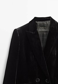Blazer en velours noir avec revers en encoche et boutons croisés, montrant une étiquette intérieure avec la marque et le texte "Made in China".