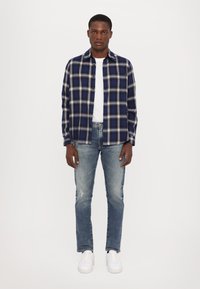 Tumesinise ja valge ruudulise mustriga särk, millel on nööbid, koos helesiniste kulunud teksade ja valgete tossudega. Sile kangas, mugav lõige.