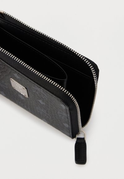 Μαύρο υφασμάτινο πορτοφόλι με φερμουάρ, μερικώς ανοιχτό, που δείχνει τις εσωτερικές θήκες και το ασημένιο φερμουάρ με μαύρη λαβή, σε λευκό φόντο.