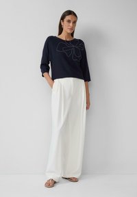 Pull marin à manches trois quarts, orné d'une broderie florale blanche ; associé à un pantalon blanc fluide et des sandales plates.