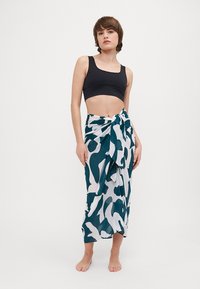 Jupe portefeuille en teal et blanc avec un motif abstrait, faite en tissu léger. Nouée à la taille, elle tombe jusqu'à mi-mollet.