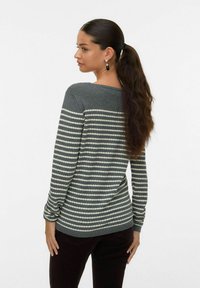 Pull en tricot gris avec des rayures blanches horizontales, encolure ronde et manches longues. Dispose d'un tissu texturé. Porté avec un pantalon sombre.