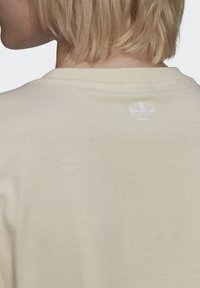 Kreminės spalvos, trumpomis rankovėmis marškiniai, pagaminti iš minkštos medvilnės, su išryškinta kaklo linija. Nugaros pusėje yra mažas siuvinėjimas su logotipu.