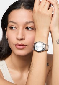 Zilveren roestvrijstalen horloge met een ronde kast, witte wijzerplaat en zilveren uurmarkers. Voorzien van een metalen schakelarmband en datumweergave.