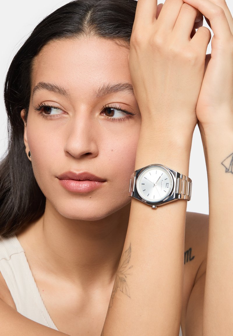 Zilveren roestvrijstalen horloge met een ronde kast, witte wijzerplaat en zilveren uurmarkers. Voorzien van een metalen schakelarmband en datumweergave.