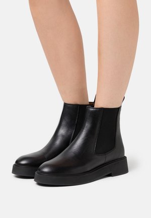 Bottines en cuir noir avec panneaux latéraux élastiques, bout rond et semelle plate en caoutchouc. Texture lisse et design minimaliste.