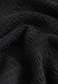 Gros plan sur un tissu noir avec des nervures texturées et des coutures horizontales créant une apparence froissée et matelassée.