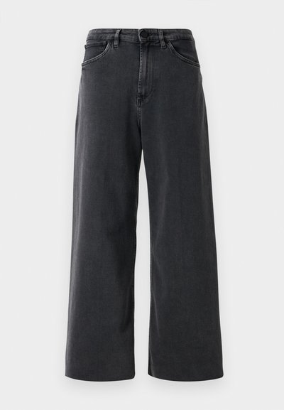 Juodų plačių džinsų kelnių su priekiniais mygtukais ir užtrauktuku, diržo kilpomis ir priekinėmis kišenėmis, fonas - balta spalva.