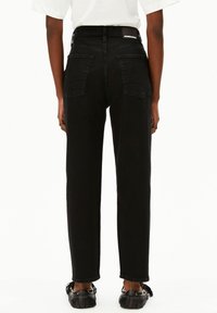 Jean noir taille haute avec une coupe droite, doté de deux poches arrière et d'une petite étiquette de marque sur la ceinture. Tissu en denim texturé.