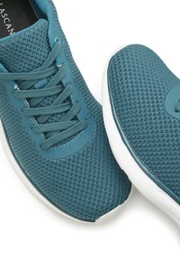 Baskets de sport teal avec une tige en maille texturée, des lacets plats et une semelle en caoutchouc. Elles présentent un embout solide et un logo sur la languette.