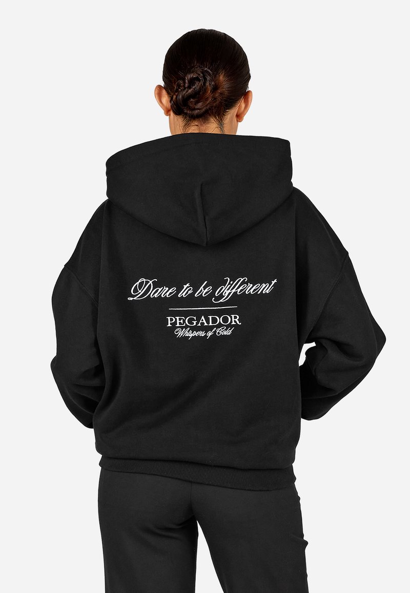 Čierna nadmerná mikina s kapucňou, s bielym textom na chrbte: "Odváž sa byť iný" a názvom značky. Mäkkučká, textúrovaná látka.