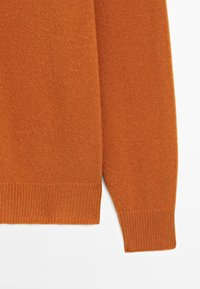 Pomarańczowy sweter z dzianiny o miękkiej fakturze, z okrągłym dekoltem oraz ściągaczami na mankietach i u dołu. Zbliżenie na tkaninę i detal rękawa.