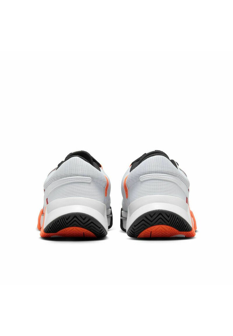 Para białych butów sportowych z czarnymi i pomarańczowymi podeszwami pokazana z tyłu na białym tle.