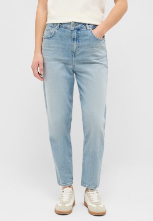 Person trägt hellblaue High-Waist-Jeans mit Fronttaschen, kombiniert mit weißen und beigen Sneakern und einem in den Bund gesteckten weißen Top.