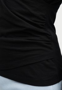 Sort figursydd topp i rynket stoff, brukt med lyseblå teksturerte bukser, som fremhever sidesøm og hemdetaljer.