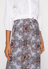 Jupe boutonnée avec un motif floral et géométrique multicolore sur fond blanc, texture lisse et cinq boutons visibles.