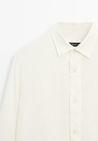 Witte linnen shirt met een klassieke kraag, sluiting met een knopenrij aan de voorkant en een subtiele textuur. Labels zichtbaar onder de kraag.