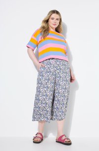 Top a maniche corte a righe nei toni del rosa, arancione e blu, abbinato a pantaloni larghi a fiori nei colori blu, giallo e rosa. Sandali rosa.