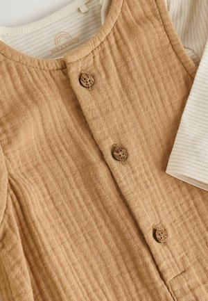 Light brown textured baby garment with three round wooden buttons over a cream and beige striped long-sleeve shirt sleeve visible.