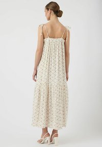 Maxiklänning i krämfärgad tyg med blommönster, justerbara knytband och en flerlagerskjol, med en svängig design och mjuk textur.