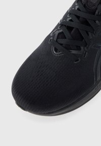 Black athletic shoe with a breathable knit upper, textured surface, and flat laces. Rounded toe and reinforced sole for support.