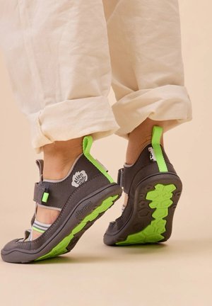 Graue Sandalen mit grünen Akzenten, verstellbaren Riemen und profilierten Gummisohlen. Mit einem Logo an der Seite und einer Lasche zum einfachen An- und Ausziehen.