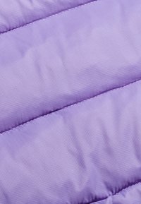 Tissu matelassé violet avec un léger éclat, présentant un motif en grille. La texture douce et les sections rembourrées créent une apparence légère et isolante.