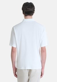 Polo shirt bianco a maniche corte realizzato in tessuto testurizzato con motivo a coste, caratterizzato da un colletto classico e un orlo dritto sul retro.