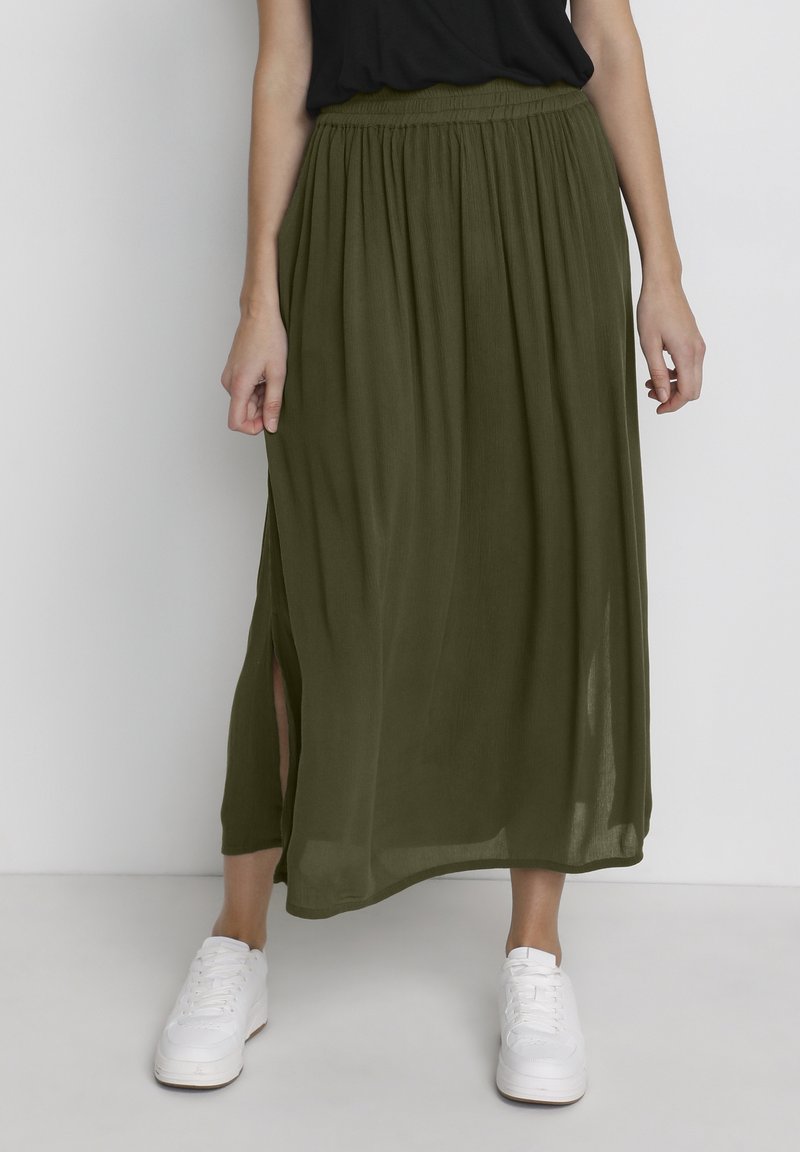 Jupe maxi vert olive en tissu léger et fluide avec une ceinture élastique et une fente latérale, portée avec des baskets blanches.
