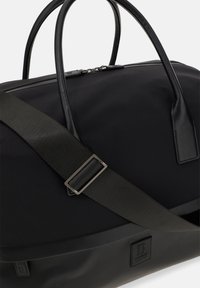 Svart duffelväska i nylon med läderdetaljer, med dubbla handtag och en avtagbar axelrem, slät yta och dragkedjestängning.