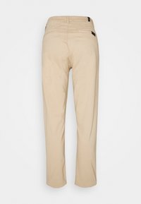 Beżowe spodnie o prostym kroju, z dwoma kieszeniami z tyłu oraz metką na pasku. Tkanina wydaje się gładka z lekką fakturą.