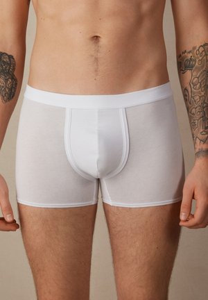 Weiße Boxer-Slips aus weichem, dehnbarem Stoff mit breitem Bündchen und enganliegendem Design, das eine Mittelnaht und keine sichtbaren Muster aufweist.