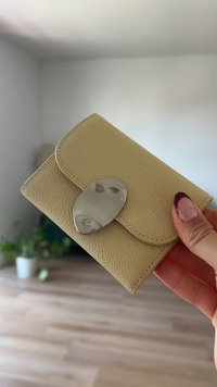 Yellow leather wallet with a textured finish, featuring a metallic oval clasp. Compact rectangular shape with rounded corners.
