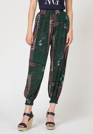 Pantalones verdes con estampado, sueltos, con puños elásticos, combinados con sandalias negras de cuña y una camiseta oscura.