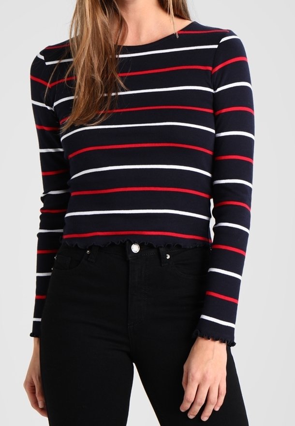 Navyrandig långärmad topp med röda och vita horisontella linjer. Har en scalloped nederkant och en figurnära design, kombinerad med svarta högmidjade jeans.