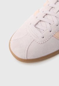 Basketbola apavi ar gaiši rozā zamšādas augšdaļu, gumijas krāsas zoli un gaiši rozā šņorēm. Aprīkoti ar dekoratīvām šuvēm un reljefa virsmu.