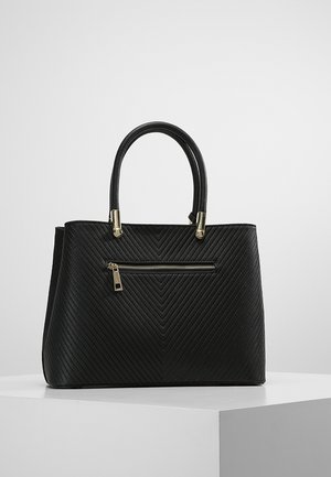 Bolso negro con textura acolchada en forma de chevron, bolsillo con cremallera dorada en la parte delantera y dos asas redondeadas, mostrado sobre superficie blanca.