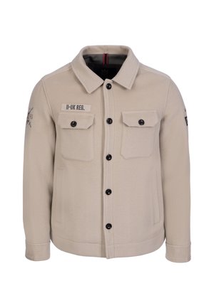 Veste beige boutonnée avec deux poches à rabat sur la poitrine, poches latérales, boutons noirs et patch texte "II-UK REG." sur la poitrine gauche.
