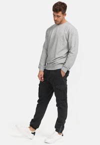 Sudadera gris con cuello redondo y puños acanalados, combinada con pantalones cargo negros con bolsillos y tobillos ajustados. Se lleva con zapatillas blancas.