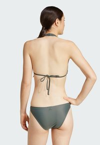 Mörkgrön bikini med halterneck-design, justerbar knytning bak och accentlogga på vänster höft. Slät textur, minimal täckning.