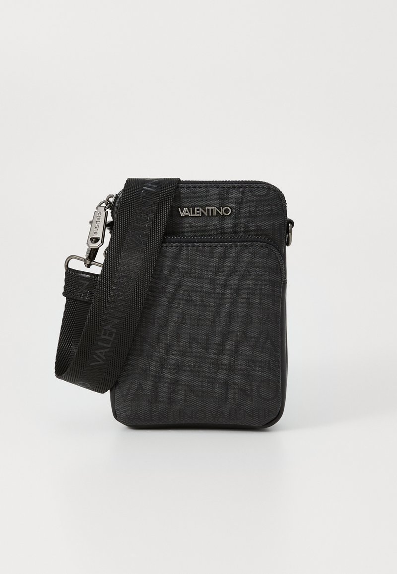 Sac bandoulière noir en tissu à surface texturée, avec logo en relief et une sangle amovible. Fermeture zippée et design minimaliste.