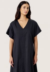 Black cotton dress with a V-neck, short sleeves, and a loose fit. Features a center seam and a slightly textured fabric.
