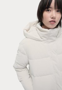 Witte pufferjack met een afneembare capuchon, gequilt ontwerp, ritssluiting aan de voorkant en zijzakken. Gladde textuur, lichtgewicht materiaal.
