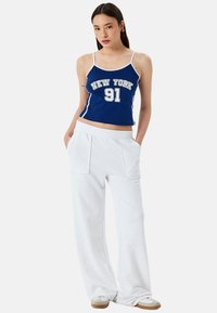 Blauwe cropped tanktop met opdruk "NEW YORK 91", gecombineerd met witte wijde sweatpants met zijzakken en een elastische tailleband.